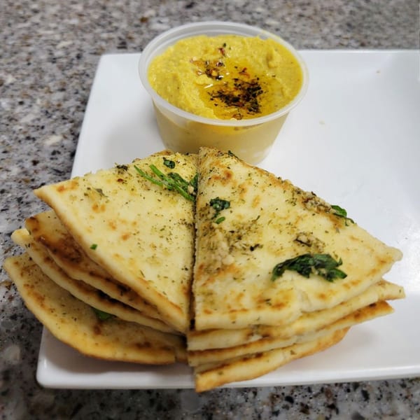 Greek pita bread with herbs and spices, served with a side of hummus drizzled with olive oil.