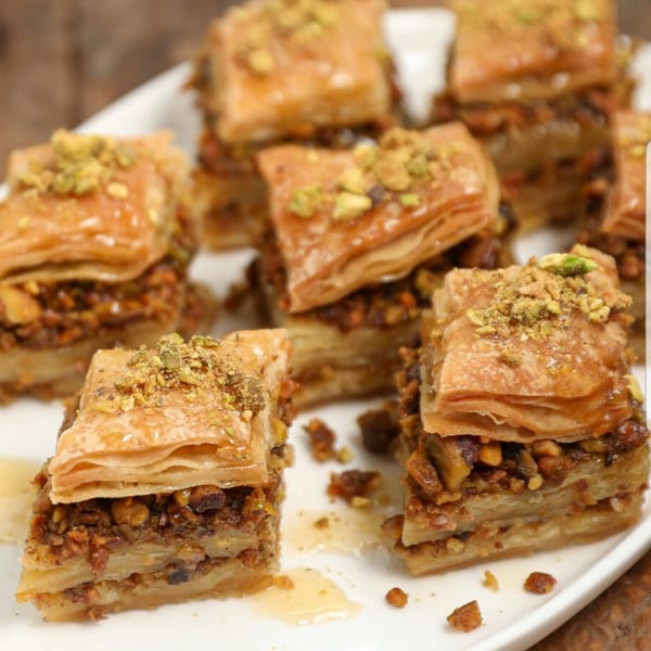 Close-up of several pieces of Greek baklava, drizzled with honey and topped with chopped pistachios.