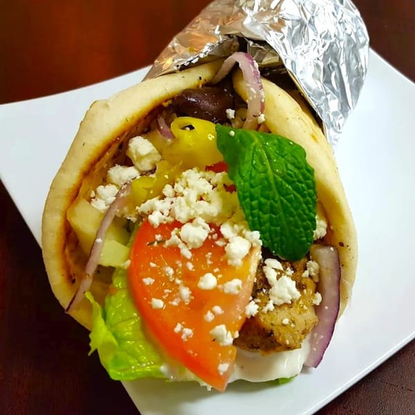 A Greek gyro with chicken, feta, tomato, lettuce, red onion, and mint, partially wrapped in foil.