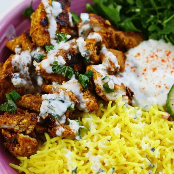 Greek chicken gyro bowl with yellow rice, tzatziki, and greens in a pink bowl.