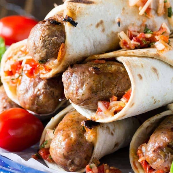 Close-up of Greek sausage wraps with salsa and tomatoes on a blue and white plate.