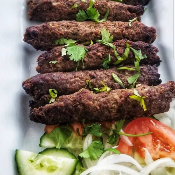 Grilled Greek kofta kebabs garnished with fresh cilantro, served with a side salad of cucumbers, tomatoes, and onions.