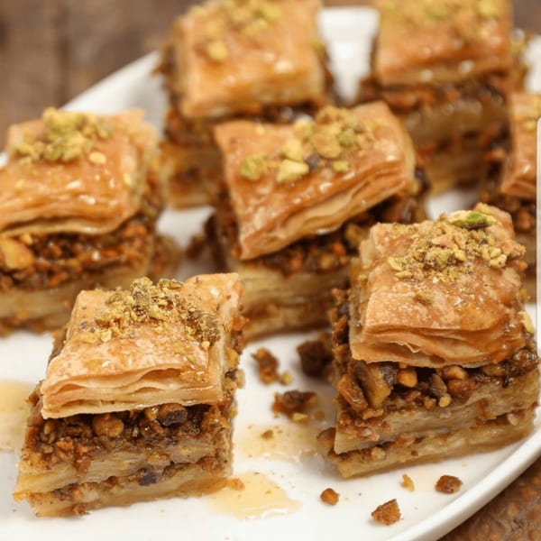 Close-up of several pieces of Greek baklava with honey and chopped pistachios on a white plate.